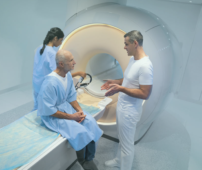 Leben mit Prostatakrebs: Ein Patient sitzt auf der Liegefläche eines MRT-Gerätes und unterhält sich mit einem Arzt. Ein Patient sitzt auf der Liegefläche eines MRT-Gerätes und unterhält sich mit einem Arzt.